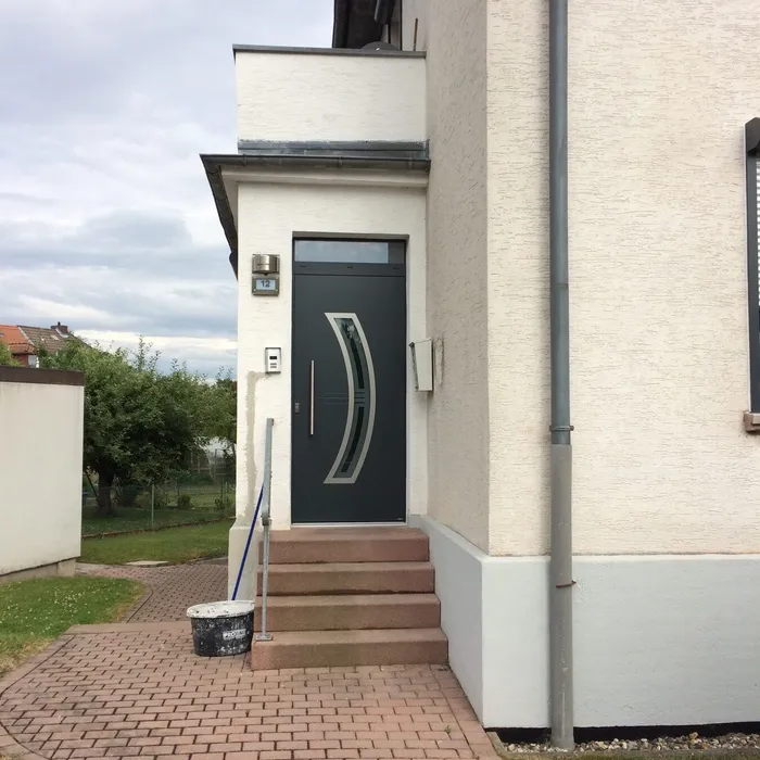 Haustür in Anthrazit mit geschwungenem Stoßgriff und gepflastertem Zugang