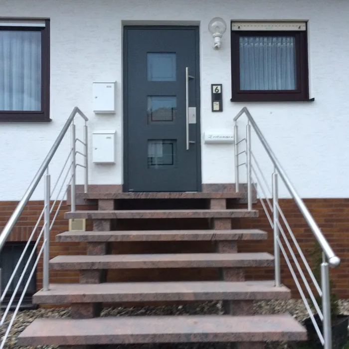 Blaugraue Haustür mit Edelstahlgeländer an der Außentreppe