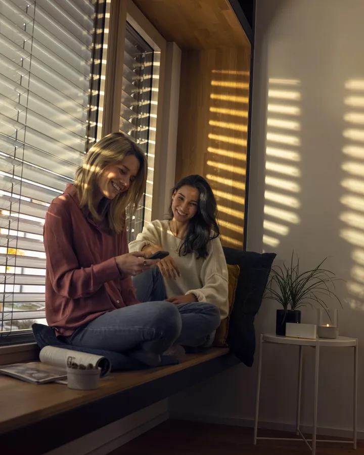 Zwei Frauen am Fenster hinter einem Raffstore mit Somfy-Antrieb